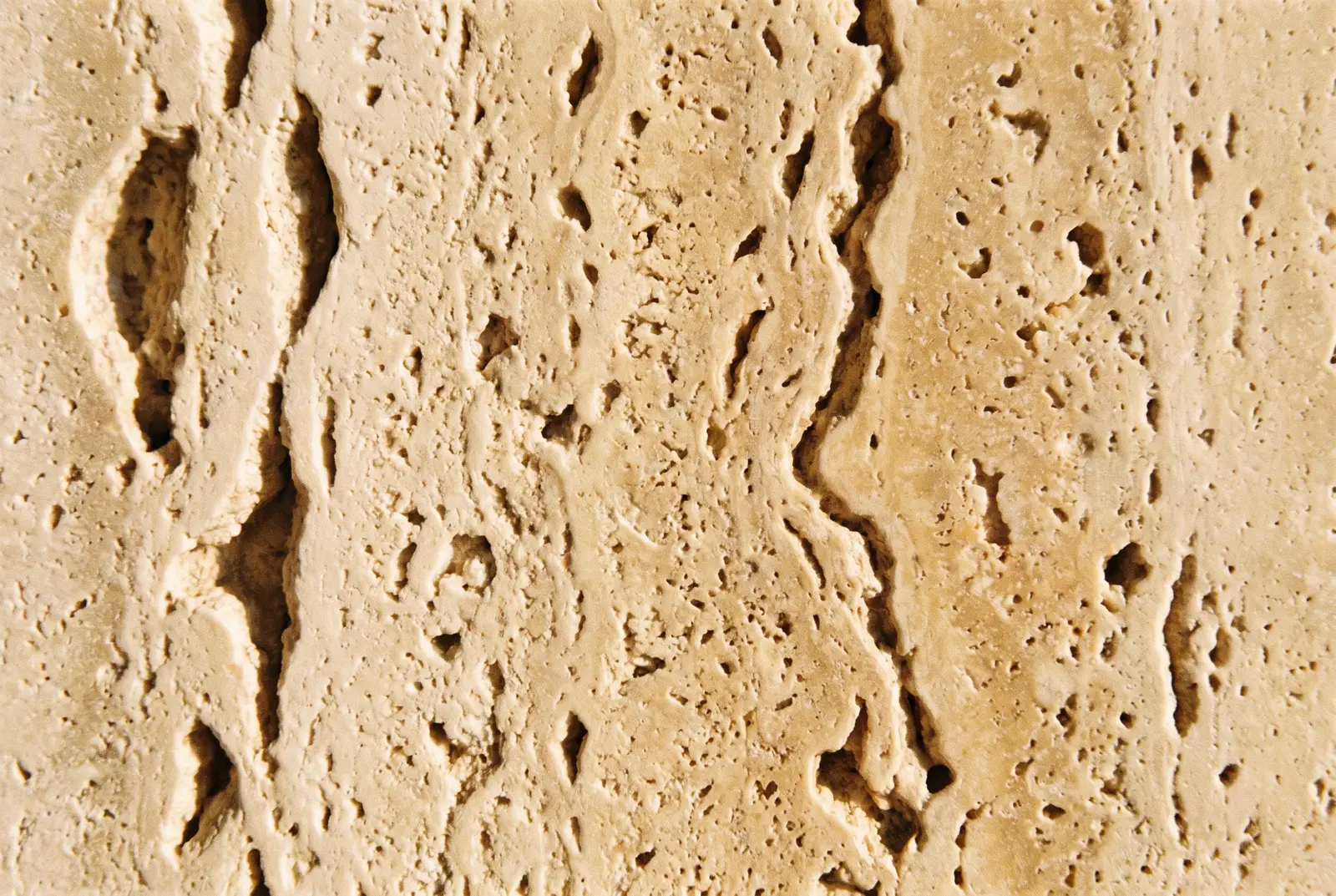 Macrotextuur van travertijn: warm crème natuursteen met open poriën